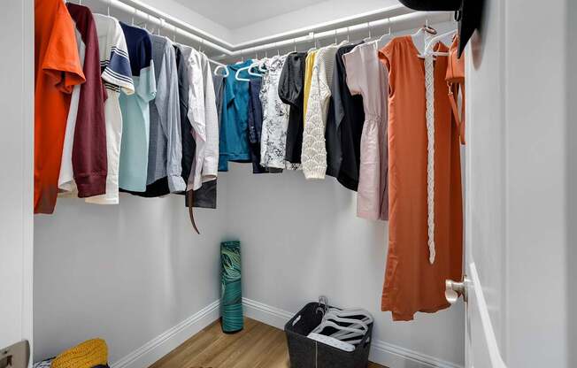 A white closet with clothes hanging and a black bag on the floor.