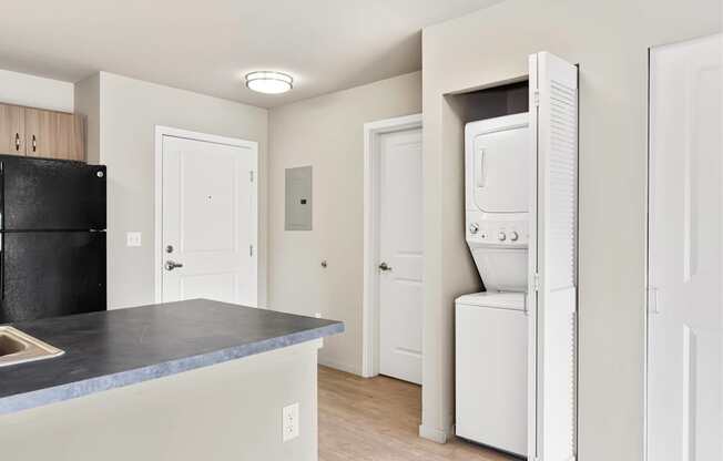 A black refrigerator sits next to a white washing machine in a kitchen.