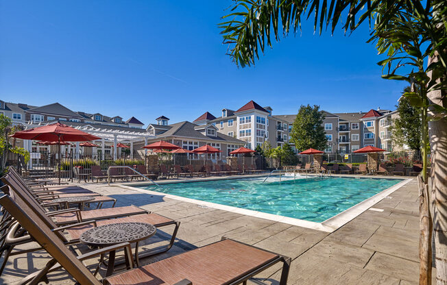 A pool area with sun loungers and umbrellas in front of apartment buildings at Vermella Lyndhurst apartments, Lyndhurst