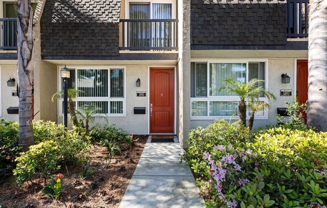 a sidewalk in front of a house with a red door