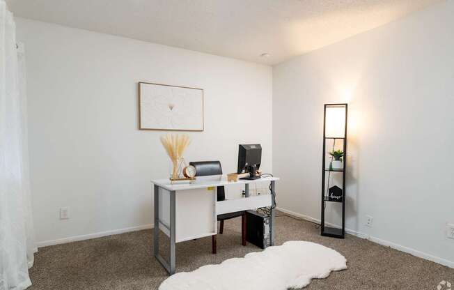 A room with a desk, chair, and a white rug.