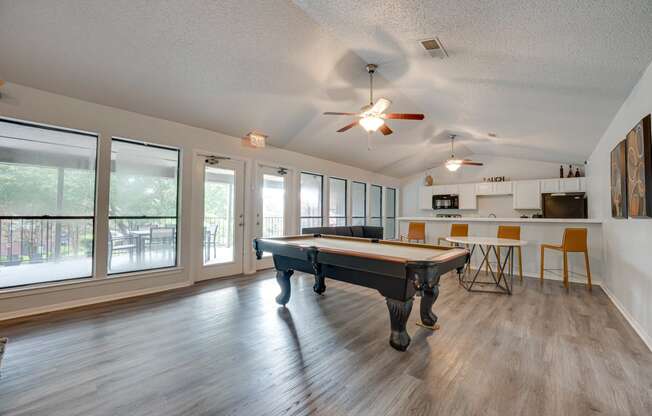 an open living room with a pool table and a kitchen with windows