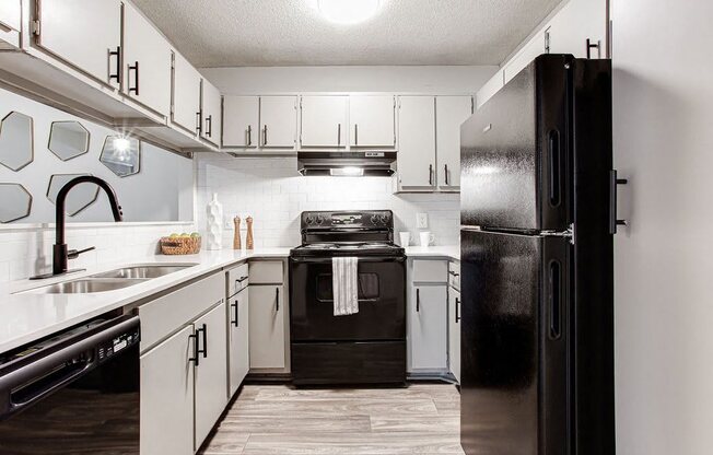 A black refrigerator stands in a kitchen with white cabinets and a black stove.