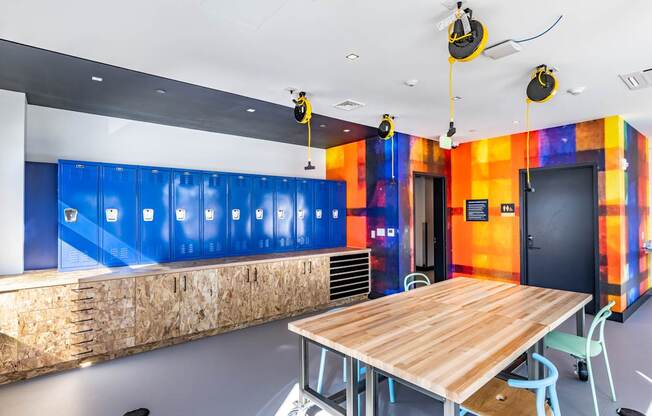 A room with a wooden table and chairs, a ceiling fan, and a wall with a blue and orange design.