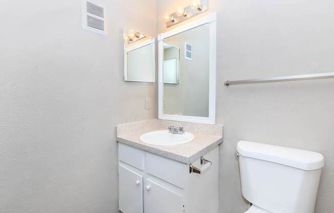 A white bathroom with a toilet, sink, and mirror.