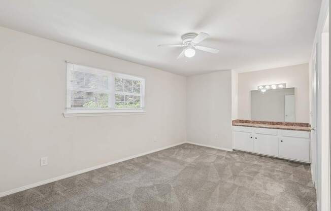 A room with a carpeted floor, a ceiling fan, and a window with blinds.