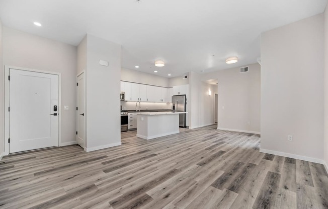 an empty living room and kitchen with white walls and wood flooring