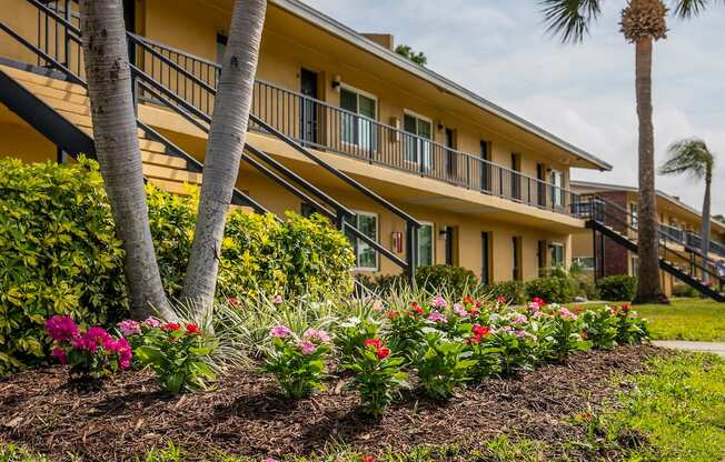 a yellow building with palm trees and flowers in front of it