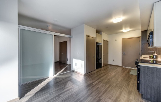 Living Room with View of Kitchen, View of Bedroom, Hardwood Inspired Floor and Black Refrigerator in Corner
