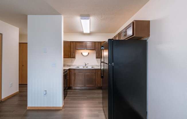 an empty kitchen with a black refrigerator and wooden cabinets. Moorhead, MN South Park Apartments