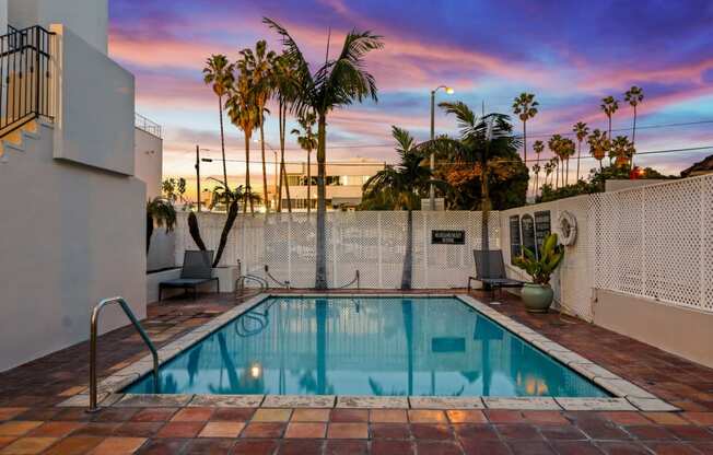 the pool of a hotel with palm trees and a colorful sky