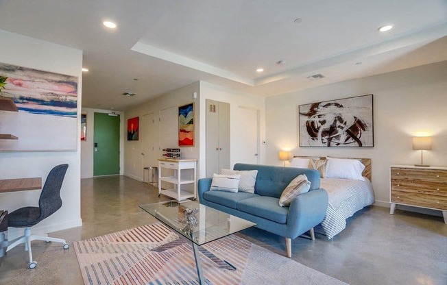 A modern bedroom with a blue couch and a glass table.