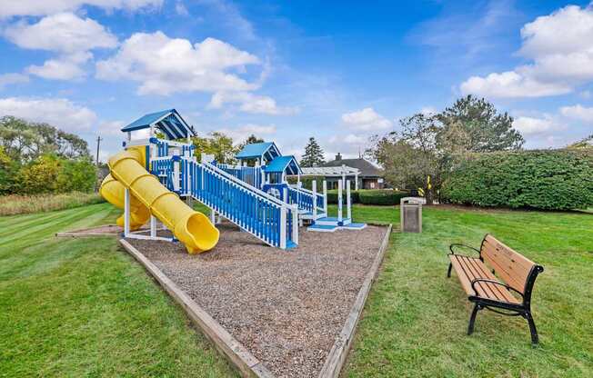 A playground with a yellow slide and a bench.