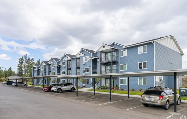 a row of blue apartment buildings with cars parked in a parking lot