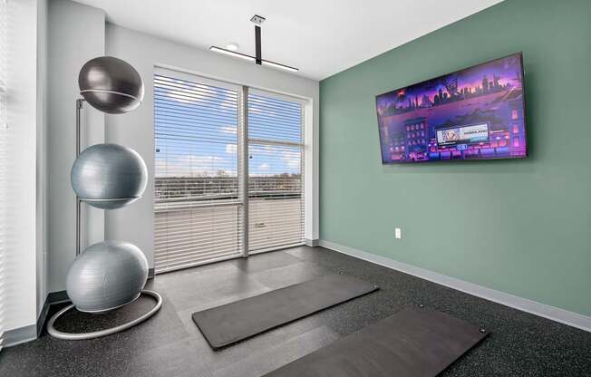 A room with a television on the wall and yoga mats on the floor.