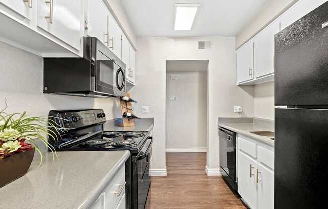 A black refrigerator is in the corner of a kitchen with white cabinets and a black stove.
