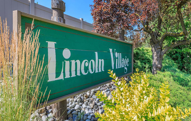 a green sign that says lincoln village with a tree in the background at Lincoln Village Apartments, Spokane Washington