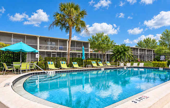 Swimming pool with lounge chairs, turquoise umbrellas and palm trees at Waterchase Apartments in Largo, FL.