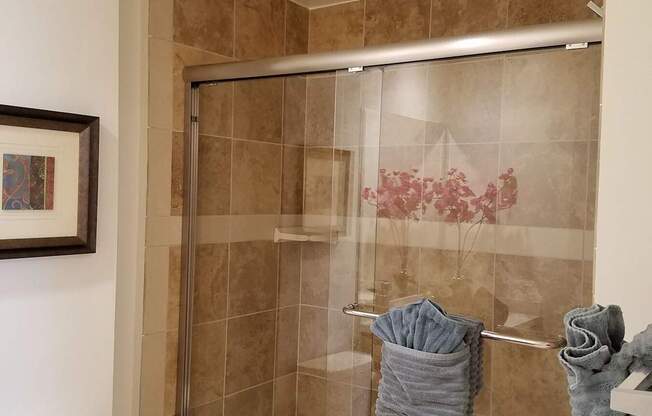 A bathroom with a toilet, a shower with a glass door, and towels hanging on a rack at Woodley Sara Apartment, Van Nuys, CA, 91406