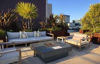 A patio with a couch, chairs, and a table with a fire pit in the middle.
