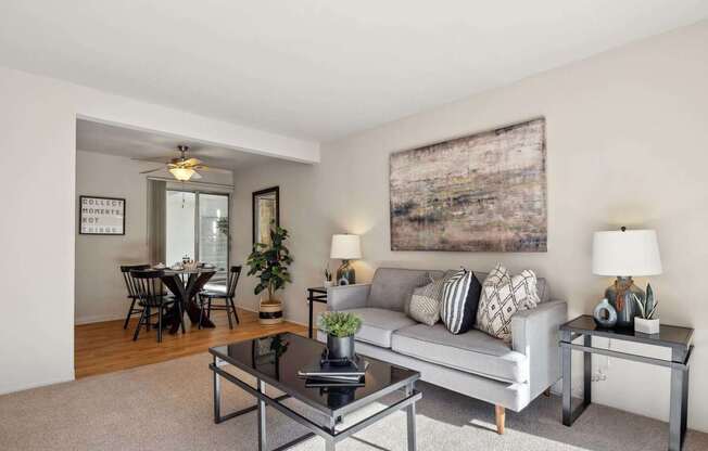 A living room with a grey couch, a glass coffee table, and a large abstract painting on the wall.