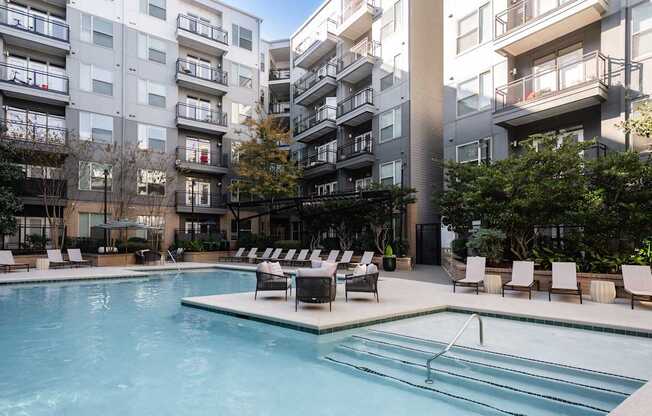 A swimming pool surrounded by lounge chairs in front of apartment buildings.