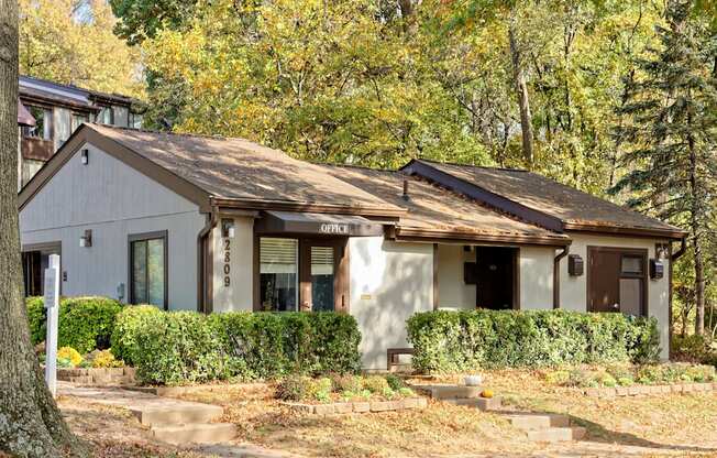 A house with a white facade and a brown roof is surrounded by greenery.