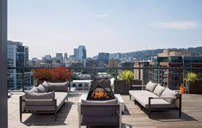 a roof deck with chairs and a fire pit overlooking a city