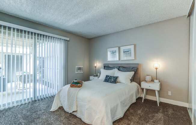 Bedroom with a Large Bed, Sliding Glass Door Leading to Patio, Carpet Flooring, and Stylish Decor at Aspire Upland Apartments, Upland, 91786