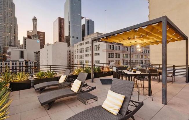 a rooftop patio with lounge chairs and a table with a view of the city