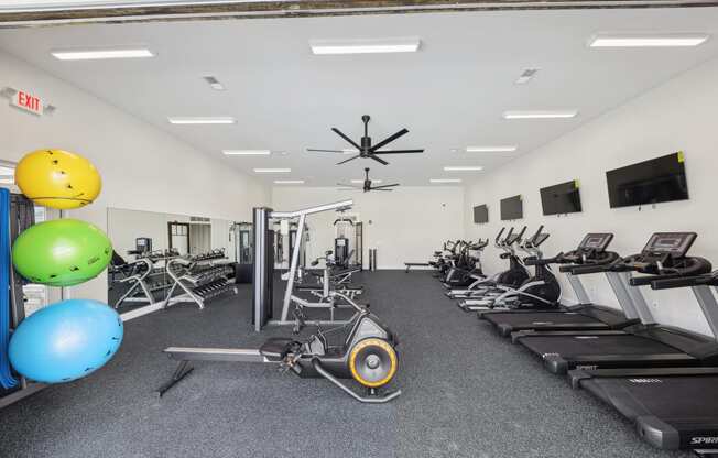 a gym with cardio machines and weights and a ceiling fan