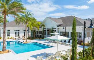 a large swimming pool with chairs and umbrellas in front of a house