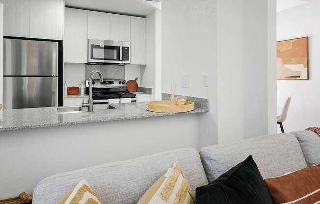 A modern kitchen with a grey couch and a stainless steel refrigerator.
