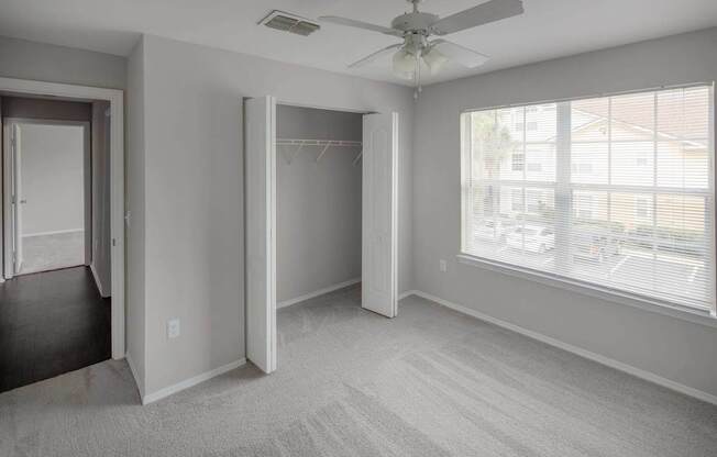 A room with a carpeted floor, a ceiling fan, and a window with blinds.