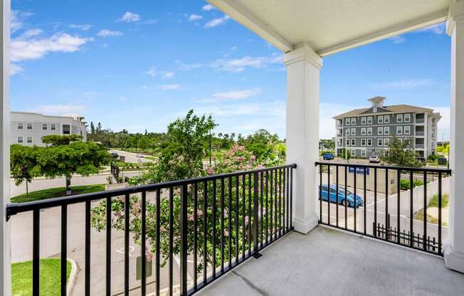 A balcony with a black railing overlooks a parking lot and buildings.