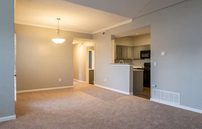 an empty living room with a kitchen in the background