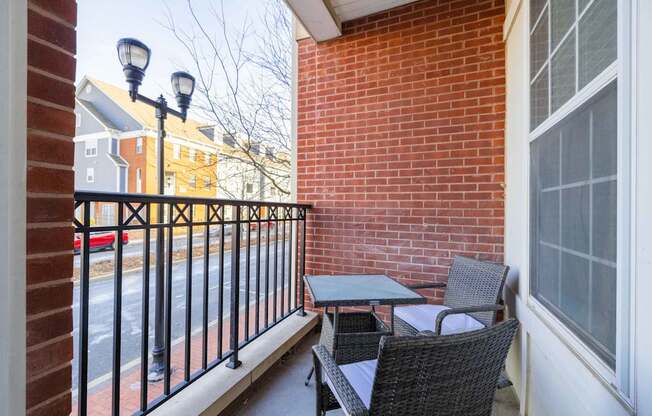 A patio with a black metal railing, a small table and chairs, and a brick wall at Harbor Pointe in Bayonne, New Jersey.