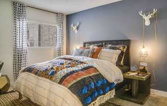 A bedroom with a bed covered in a quilt and a deer head on the wall.