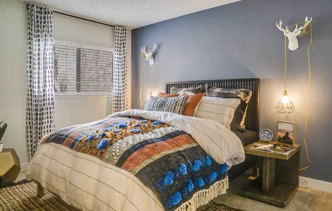 A bedroom with a bed covered in a quilt and a deer head on the wall.