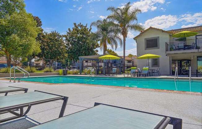 a swimming pool with tables and umbrellas in front of a house