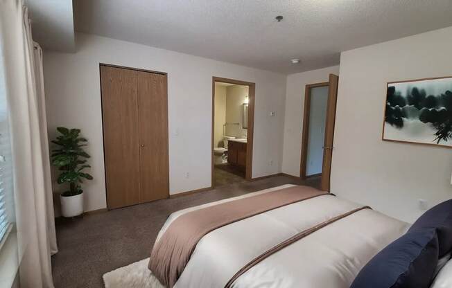 A bedroom with a bed, a plant, and a painting on the wall.
