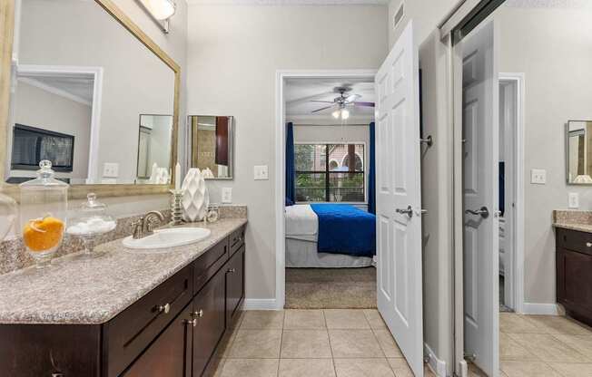 A bathroom with a sink, mirror, and a bed in the background.