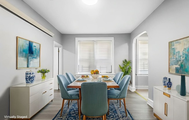 A dining room with a table set for six and a blue rug on the floor.