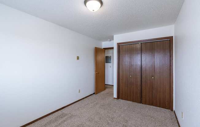 a bedroom with carpet and a door to a closet. Fargo, ND Plumtree Apartments