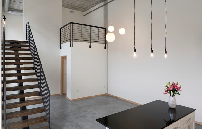 A room with a staircase, a table with a vase of flowers, and hanging lights.
