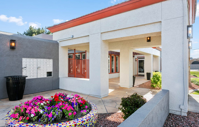 a white building with a red roof and a large planter with colorful flowers