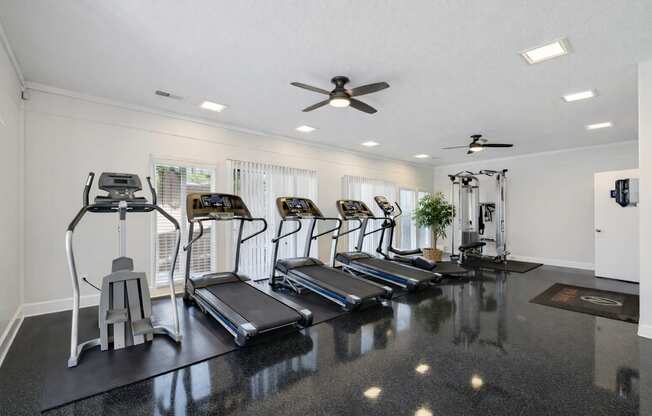 A spacious home gym with treadmills, elliptical machines, and a fan.