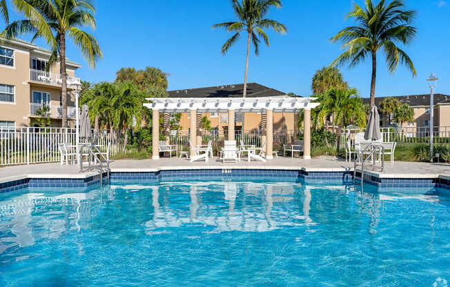 A pool with a white pergola and palm trees in the background.