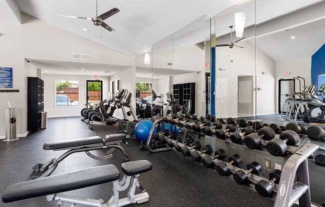 Spacious fitness center with free weights, cardio machines, mirrored wall, and vaulted ceiling.