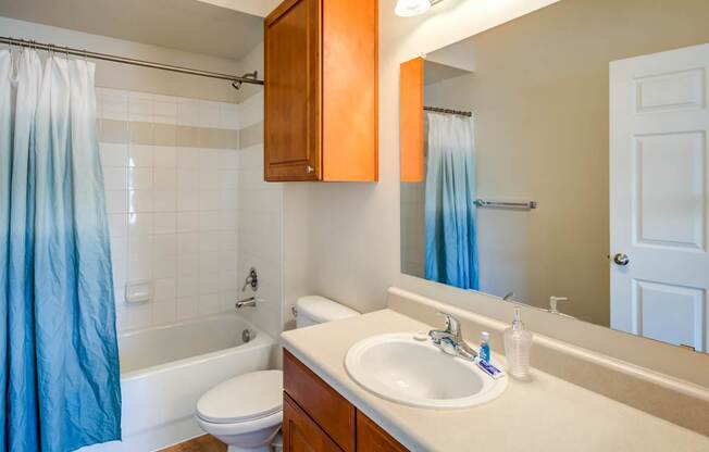 A bathroom with a white toilet, a white sink, and a white bathtub with a blue shower curtain.